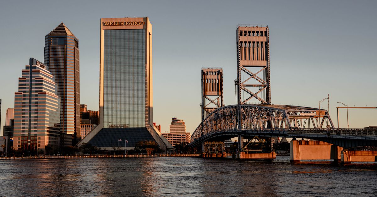 Stunning view of Jacksonville, FL skyline at sunset with iconic bridges and modern skyscrapers reflecting on the water.